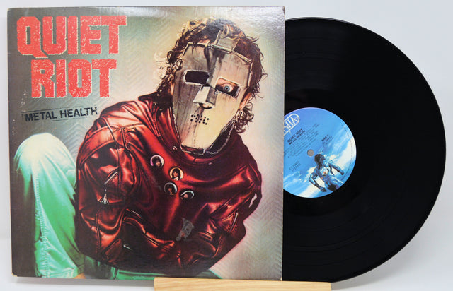 Vinyl record with 'Quiet Riot' album cover featuring a person in a red outfit and mask.
