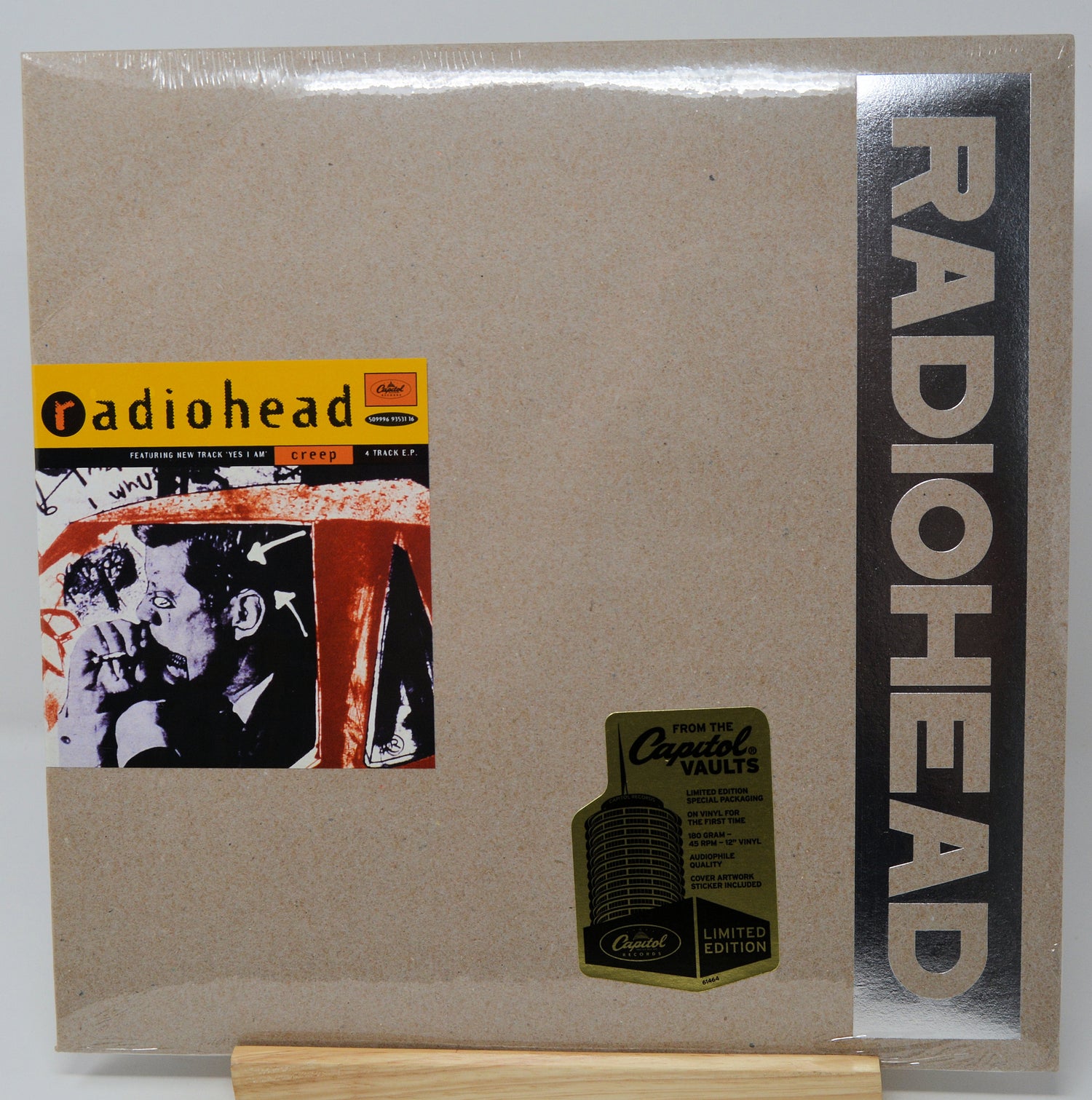 Radiohead 'Creep' 12-inch vinyl record cover, sealed in plastic and displayed on a wooden stand. The cover is a textured tan/kraft color with a vertical black band on the right featuring the white RADIOHEAD logo, a yellow and black 'Creep' album art sticker on the left, and a gold 'Capital Vaults Limited Edition' sticker near the bottom.