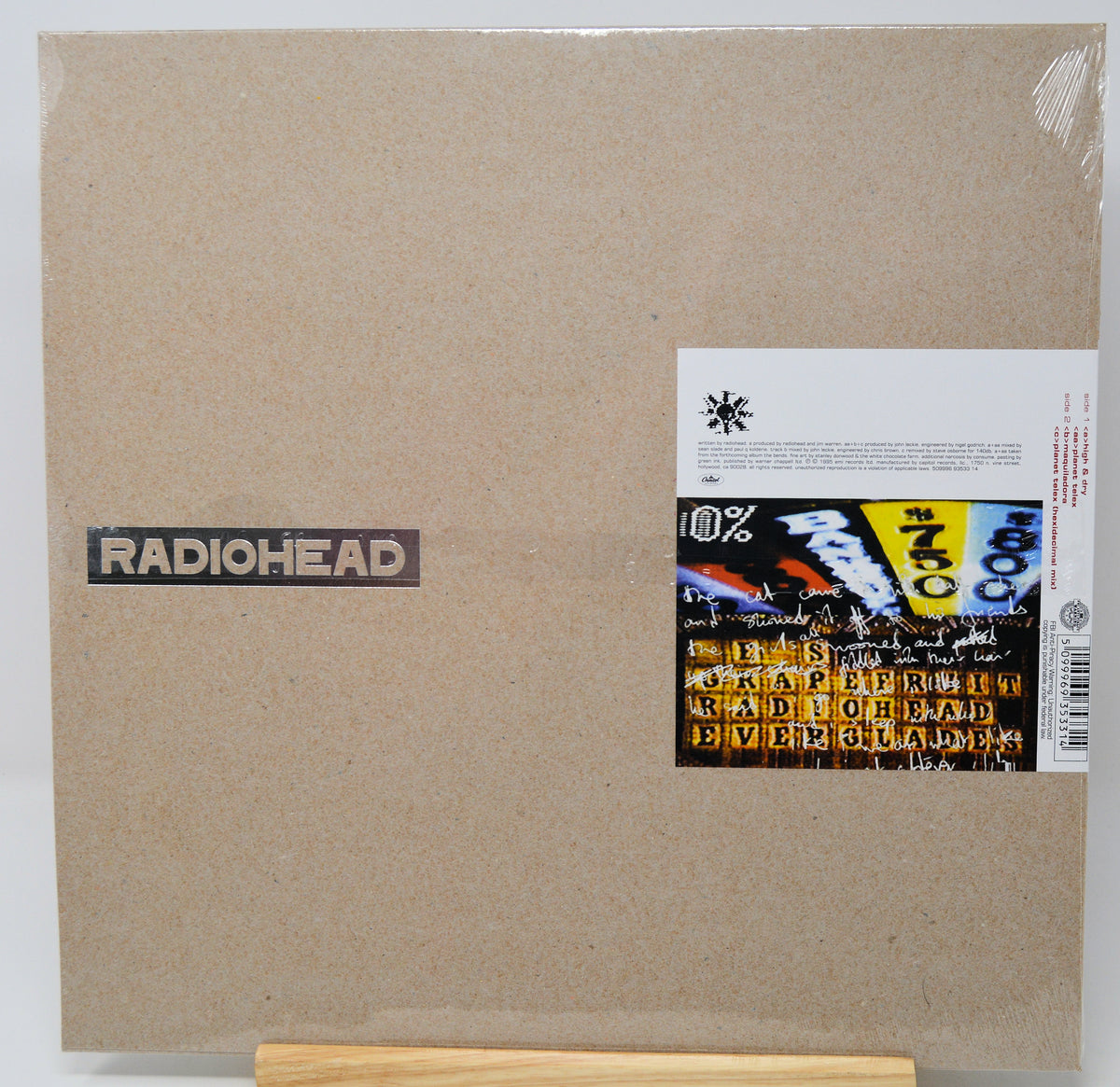Radiohead 'The Endless Peace' vinyl record album in its original cardboard brown sleeve, sealed in plastic with a sticker label on the right side, displayed on a wooden stand.