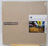 Radiohead 'The Endless Peace' vinyl record album in its original cardboard brown sleeve, sealed in plastic with a sticker label on the right side, displayed on a wooden stand.