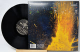 Radiohead 'Rainbows' vinyl record shown with the black LP partially pulled from the back cover, which features a dark blue and bright yellow-orange abstract splash design.