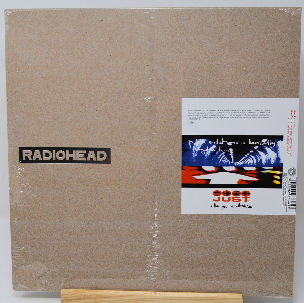 Radiohead 'The Guilty Mind' vinyl record LP in its original shrink wrap, displayed on a small wooden stand. The cover features a textured brownish-beige background with the black and white RADIOHEAD logo on the left and the album artwork on the right.