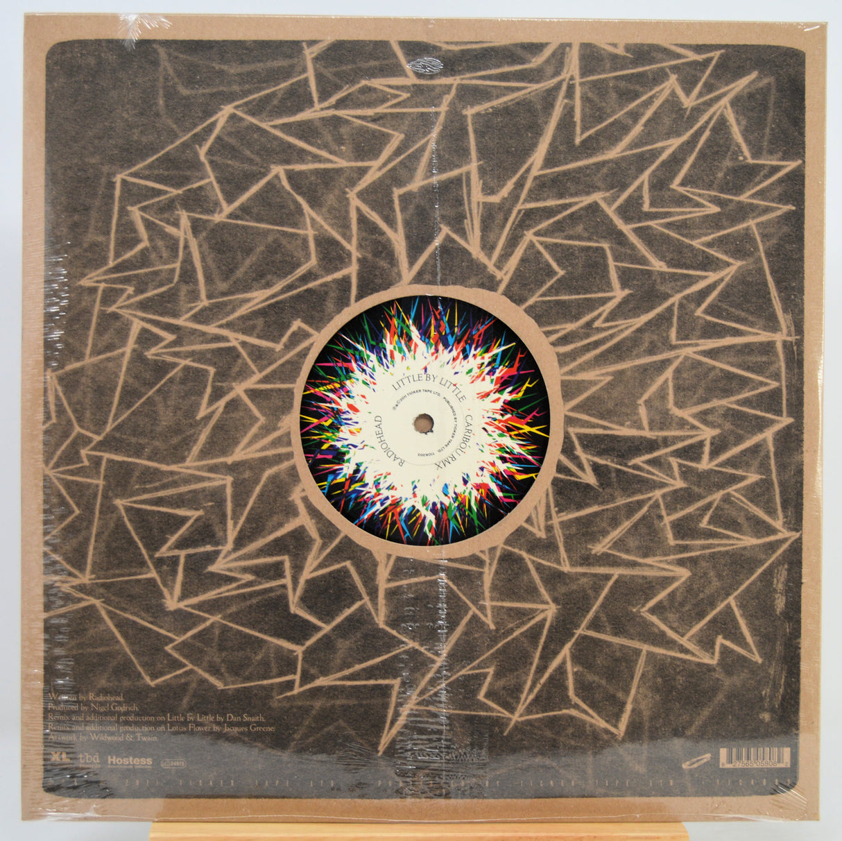 Vinyl record LP in shrink wrap with abstract geometric artwork in tan and black, featuring a colorful circular center label. The record label is visible in the center.