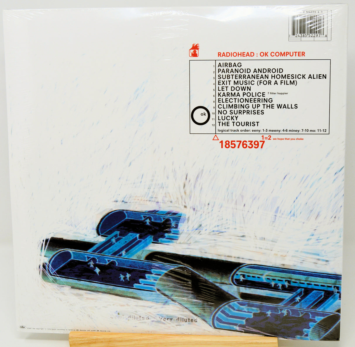 Radiohead 'OK Computer' vinyl record album cover, shrink-wrapped and photographed from above. The white cover features the band name and tracklist in black and red text, with a blue and black abstract jet graphic across the lower portion.