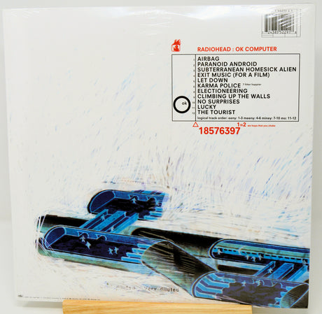 Radiohead 'OK Computer' vinyl record album cover, shrink-wrapped and photographed from above. The white cover features the band name and tracklist in black and red text, with a blue and black abstract jet graphic across the lower portion.