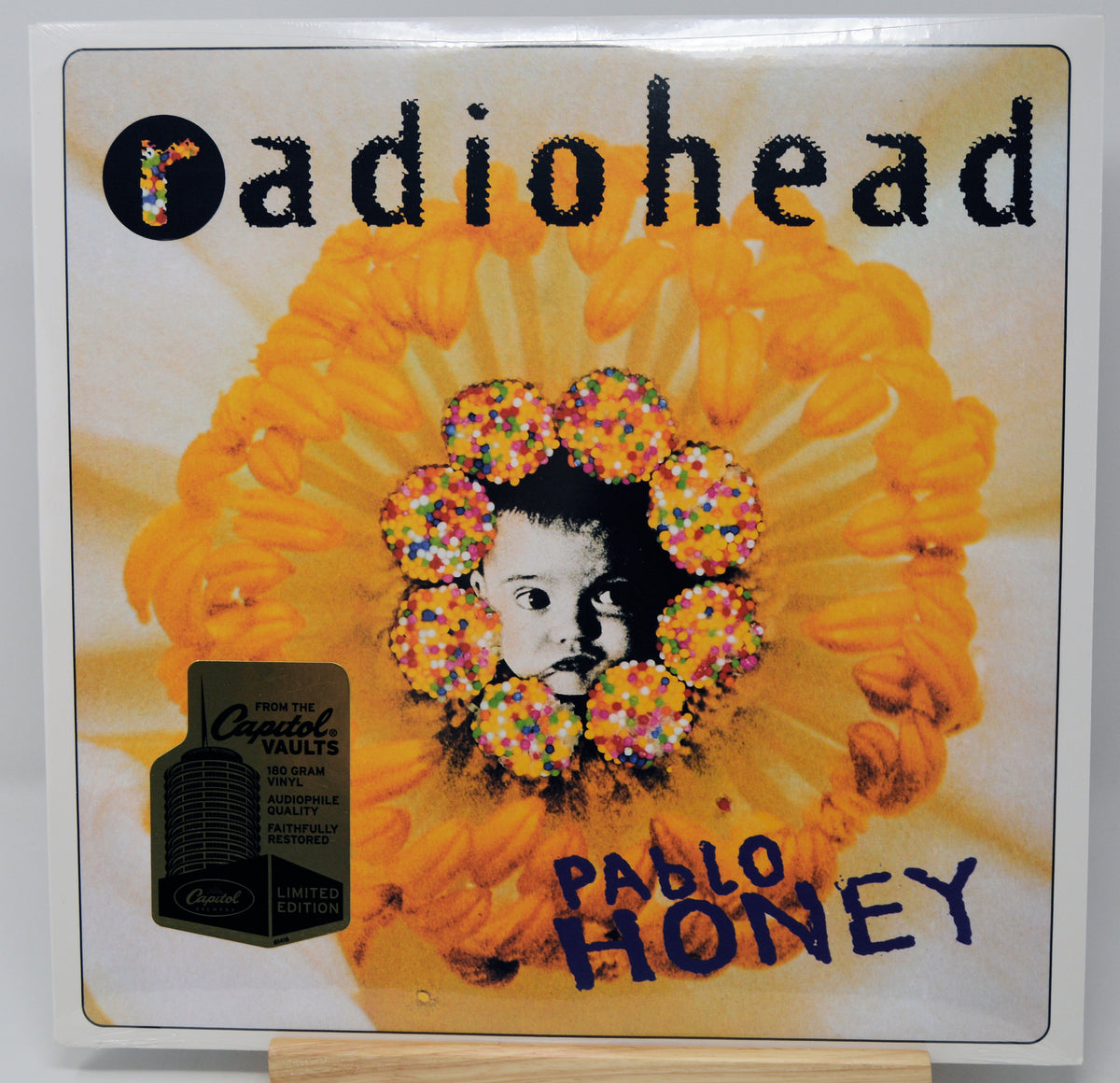 Radiohead 'Pablo Honey' vinyl record cover, featuring a large yellow flower with a central black-and-white portrait and colorful sprinkle-like circular accents. A black sticker on the left reads 'From the Capital Vaults Limited Edition.
