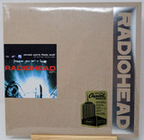Radiohead 'EP1' vinyl record cover in its original shrink wrap, displayed on a small wooden stand. The cover features a textured brown kraft-paper background, a vertical black band on the right with 'RADIOHEAD' in large silver letters, and a black square album art label on the left.