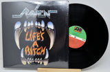 A vinyl record album for the band Raven's 'Life's A Bitch' on two records, with the black LP disc partially pulled from the sleeve. The sleeve features a black background with a graphic of metallic silver fangs and orange text.