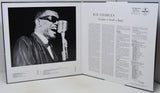An open book or magazine spread showing a black-and-white photograph of Ray Charles singing into a microphone on the left page, with article text about Ray Charles on the right page.