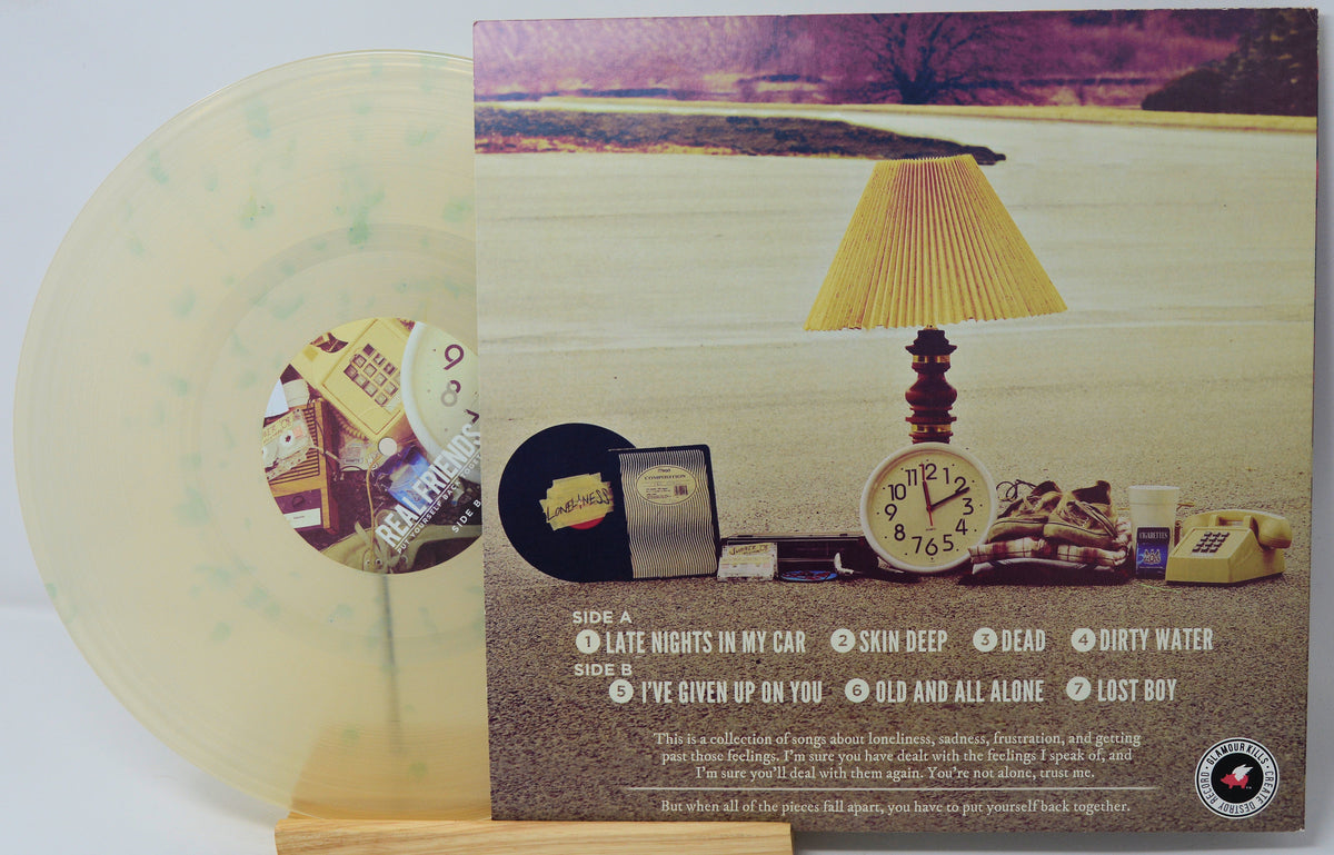 A vinyl record album shown with its printed cover art and a translucent pale yellow record partially visible behind it. The cover features a scenic landscape and a table scene with a lamp, clock, books, and a phone, with track listing text at the bottom.