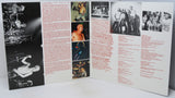 An open tri-fold booklet or printed program spread on a white surface, featuring black-and-white concert photographs, small color photos, columns of red and black text, and a few small printed images.