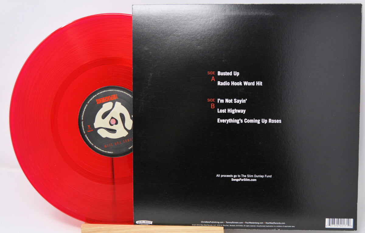 A red vinyl record partially pulled from its black outer sleeve, photographed on a white background. The sleeve shows tracklist text for 'Busted Up', 'Radio Hook Word Hit', 'I'm Not Sayin'', 'Lost Highway', and 'Everything's Coming Up Roses'.