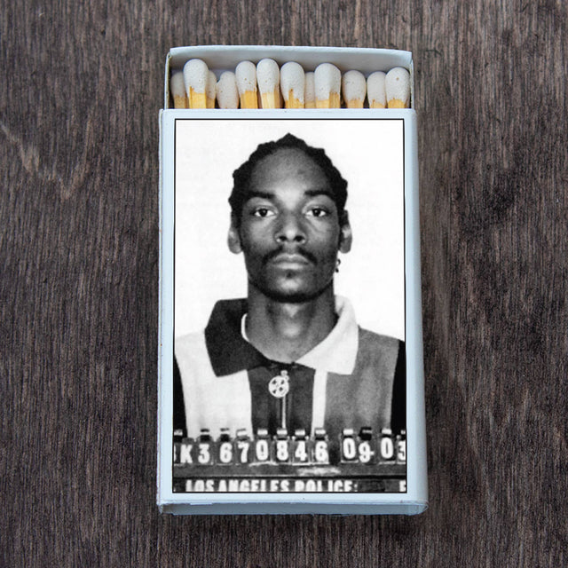 A retro-style matchbox featuring a black and white mugshot on the cover, shown on a wooden surface.