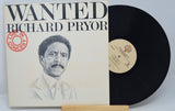 A vinyl record titled 'Wanted Richard Pryor' with an illustration of Richard Pryor on the cover, placed next to its case.