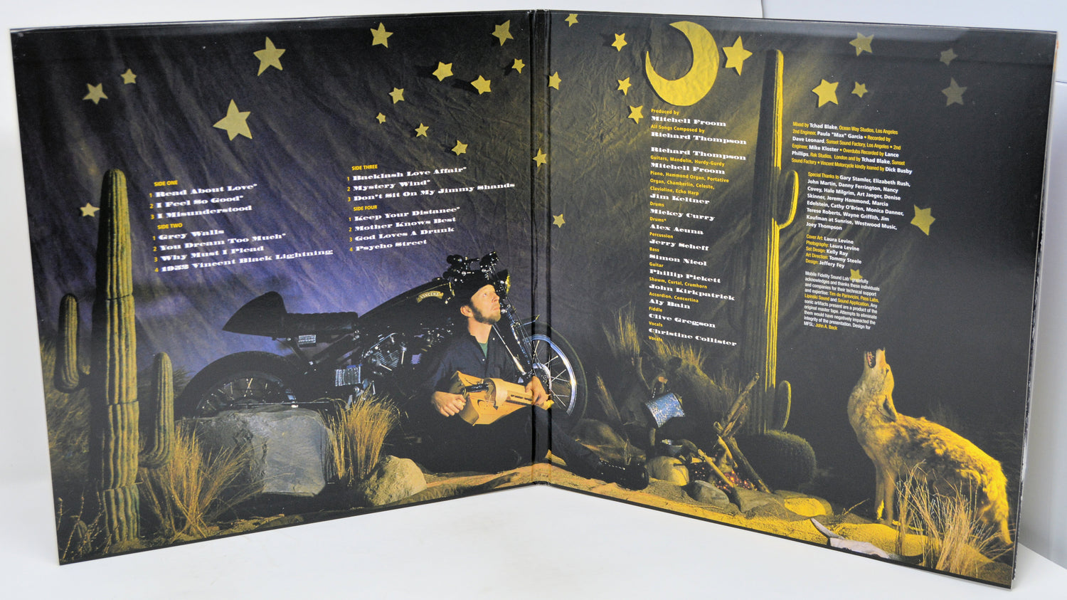 An open vinyl record sleeve or booklet displaying printed desert night artwork with a motorcycle, cactus, moon, stars, and a wolf, alongside song lists on both sides.