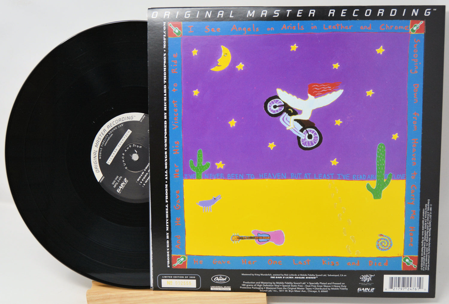 A vinyl record partially pulled from its illustrated outer sleeve, photographed on a light background. The sleeve reads 'Original Master Recording' and shows a colorful desert scene with a motorcycle, cacti, stars, and a purple sky.