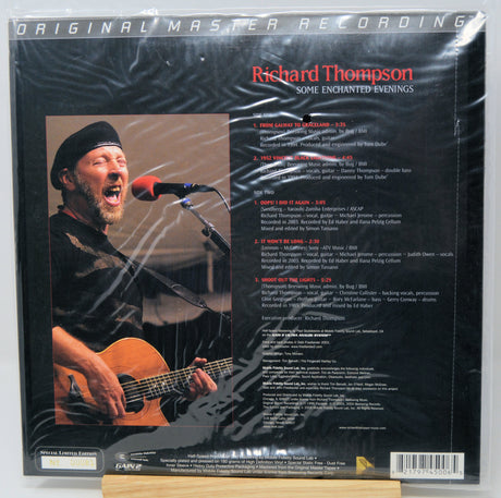 Back cover of Richard Thompson's 'Some Enchanted Evenings' 12-inch vinyl LP, sealed in plastic shrink wrap. The black cover features a photo of the singer performing live with an acoustic guitar and a track list on the right.
