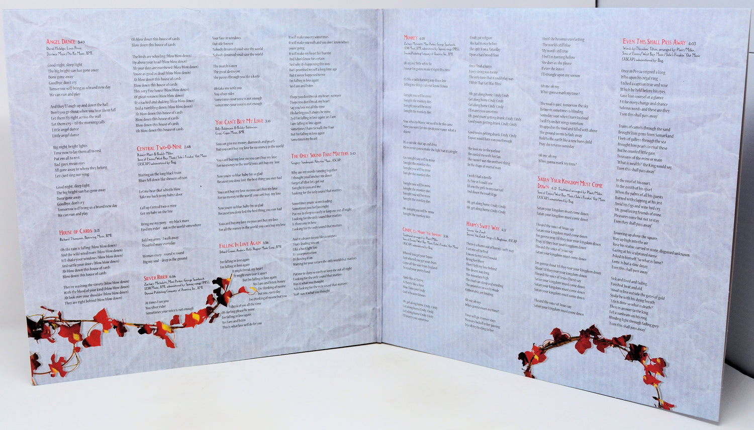 An open three-panel accordion-style booklet or program spread on a white surface, printed with many small text blocks and decorated with red and orange floral garlands along the bottom corners.
