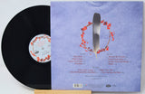 A vinyl record partially pulled from its sleeve, showing the black record and the back cover artwork with a pale lavender background, a silver knife, and red floral accents.
