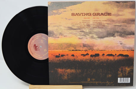 A vinyl record partially pulled from its sleeve, showing the black record on the left and the album cover on the right. The sleeve features a landscape illustration of a grassy field at sunset with a herd of cattle and the title 'SAVING GRACE' at the top.