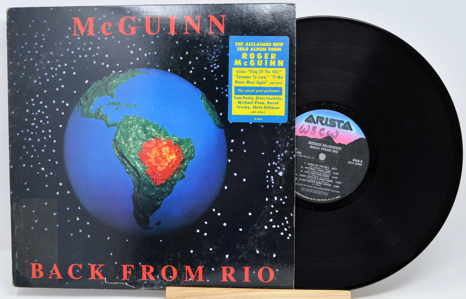 McGuinn's 'Back From Rio' vinyl record LP with its cover jacket and the black record partially pulled out, displayed on a small wooden stand against a white background.