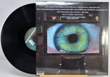 Vinyl record album with the black record partially visible behind the printed cover, showing a large green-and-blue eye on the front artwork.