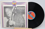 Vinyl record and cover featuring Jimmy Rogers with a jazz instrument, on a light gray background.