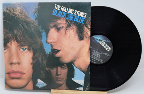 The image shows a vinyl record titled 'Black And Blue' by The Rolling Stones. The record is placed upright with its label visible, displaying the band members and the album title.
