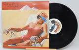 The image shows a used vinyl record of 'Rolling Stones - Made In The Shade' with a picture of a female figure in a bikini, sunglasses, and a hat, lounging in a chair.