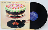 Rolling Stones 'Let It Bleed' vinyl record album with the illustrated cover on the left and the black LP record partially pulled out on the right, photographed against a plain light background.