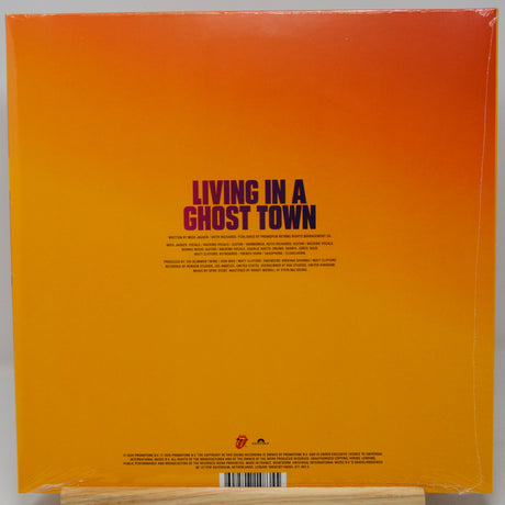 The back cover of a vinyl record for the band Living in a Ghost Town, featuring a bright orange-to-yellow gradient background with dark purple text and the band's logo at the bottom.