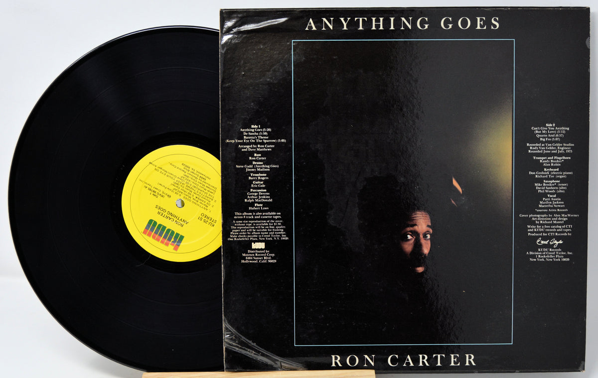 A vinyl record partially pulled from its sleeve for the album 'Anything Goes' by Ron Carter. The black record has a yellow label, and the sleeve features a dark cover with the album title at the top and the artist's name at the bottom.