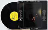 A vinyl record partially pulled from its sleeve for the album 'Anything Goes' by Ron Carter. The black record has a yellow label, and the sleeve features a dark cover with the album title at the top and the artist's name at the bottom.