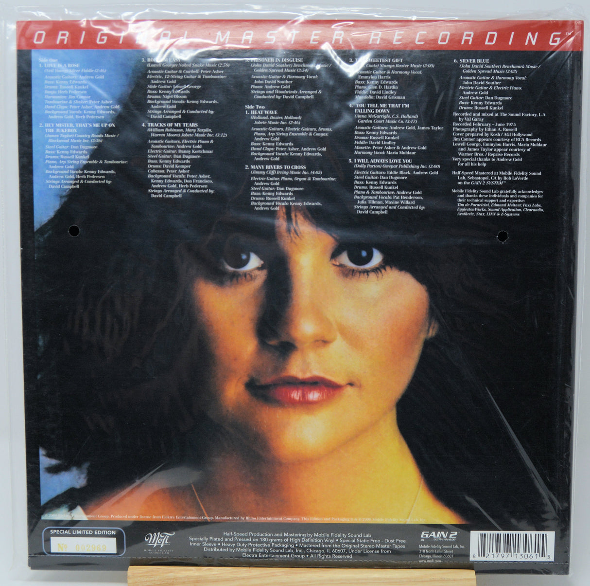 The back cover of a vinyl record album, sealed in plastic shrink wrap. The cover features a close-up portrait of a woman with dark hair against a black background, with extensive track listing text printed in columns.