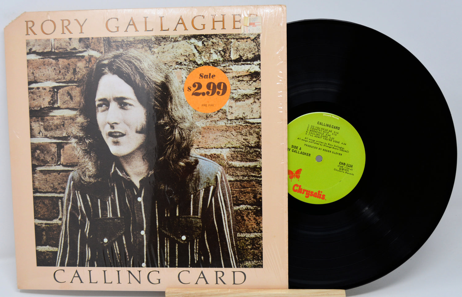 Vinyl record with cover featuring a person against a brick wall, on a light gray background.