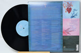 Vinyl record album shown with the black LP partially pulled from the back cover, which features a blue gradient center, song lyrics, and a pink-and-blue illustrated side panel. The record label reads 'The List'.