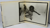 Open book with a black and white photograph of a person on a bed inside.