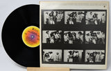 Vinyl record with a black cover featuring black and white photos of a band, on a light gray background.