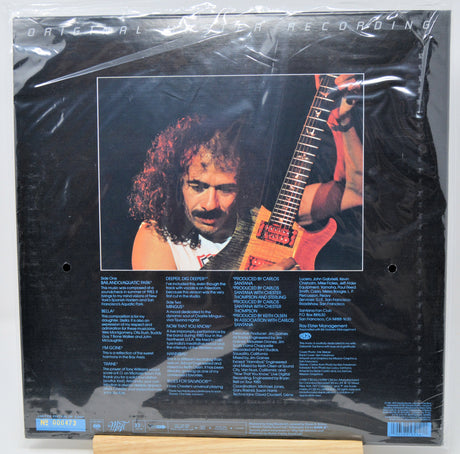Vinyl record album back cover under shrink wrap, featuring a black background with a large portrait of a guitarist and track listing text below.