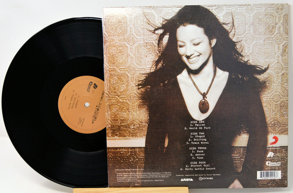 A vinyl record partially pulled from its album jacket, showing the black LP disc and the printed cover art. The cover features a portrait of a smiling woman against a patterned beige background, with track listing text on the lower right.