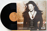 A vinyl record partially pulled from its album jacket, showing the black LP disc and the printed cover art. The cover features a portrait of a smiling woman against a patterned beige background, with track listing text on the lower right.