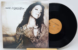 A vinyl record album for Sarah McPhaul's album 'atlonglow' shown with its illustrated cover sleeve and a black LP record partially pulled out, resting on a small wooden stand against a light gray background.