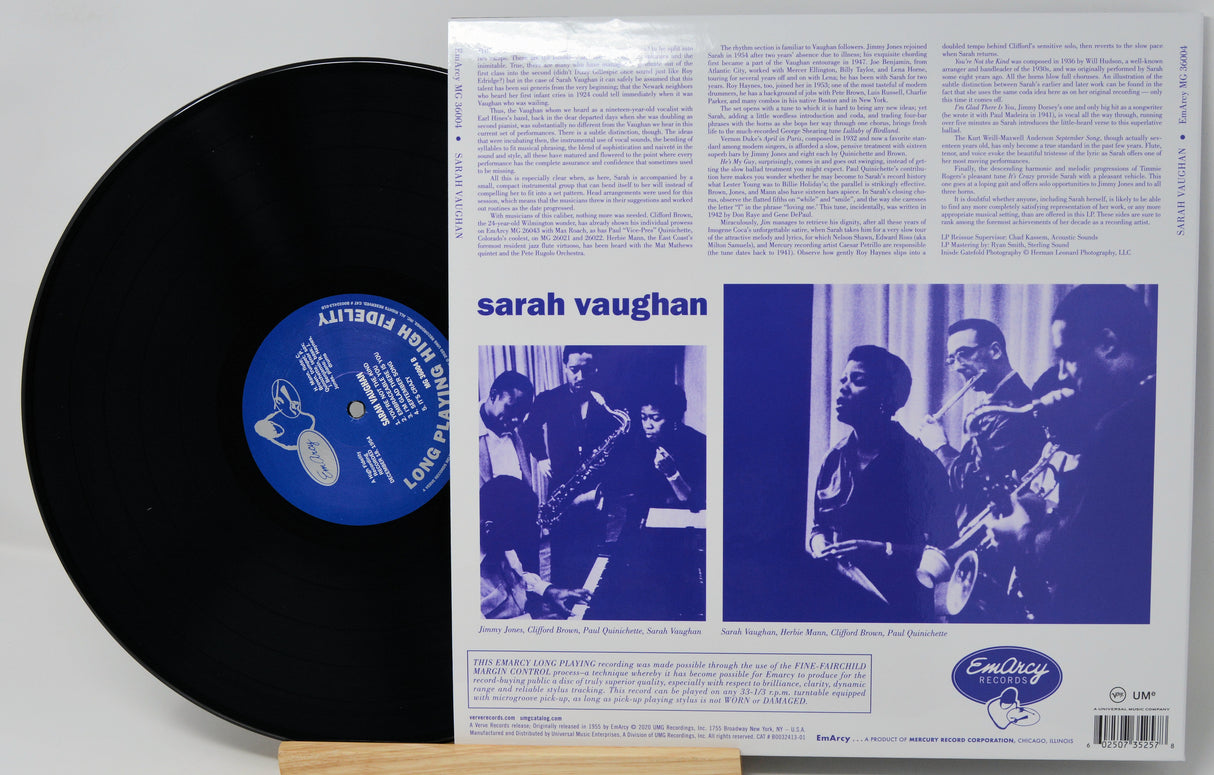 A vinyl record partially pulled from its back cover sleeve, showing the black record with a blue center label next to the printed album back cover for Sarah Vaughan's 'Love Is A Drug'.