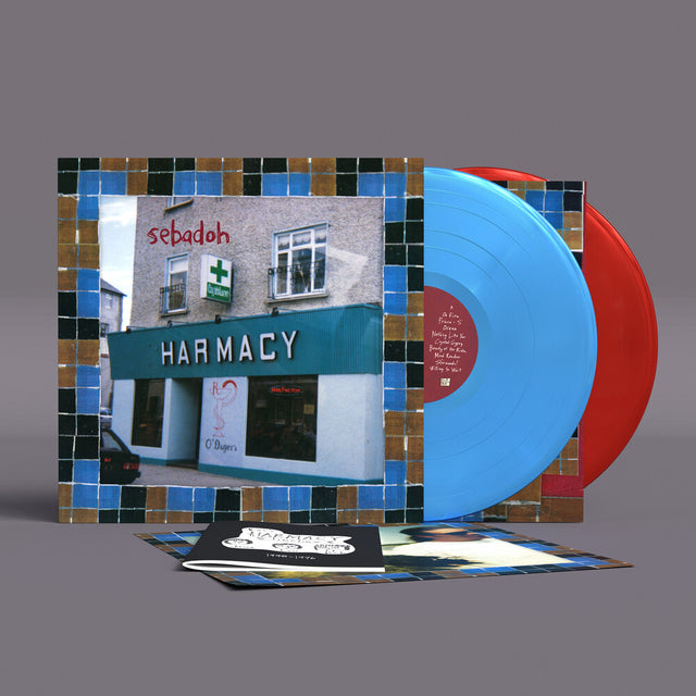A vinyl record album set displayed on a gray background, featuring a square illustrated cover with a pharmacy storefront scene and blue mosaic tile borders, a bright blue record, a red record, and printed inserts in front.