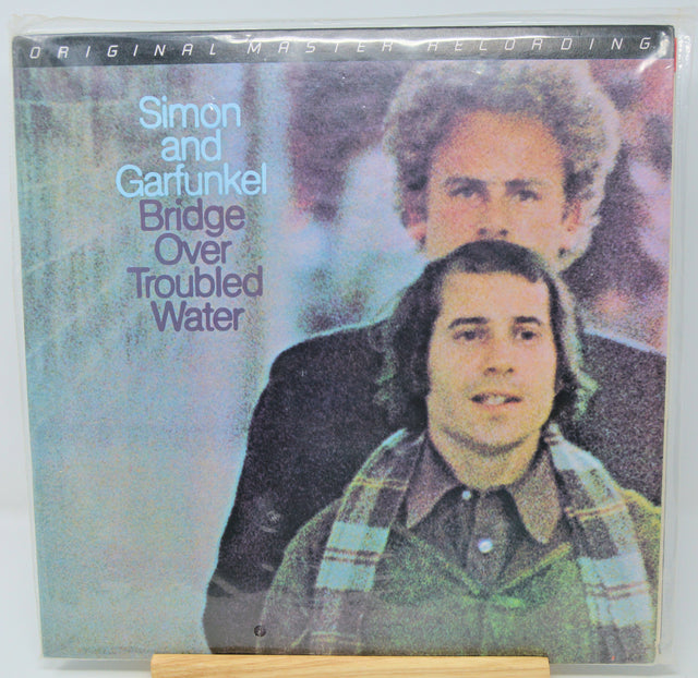 Vinyl record cover for 'Bridge Over Troubled Water' by Simon and Garfunkel with two men on a foggy bridge.