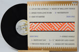Vinyl record with cover displaying track listings on a light gray background