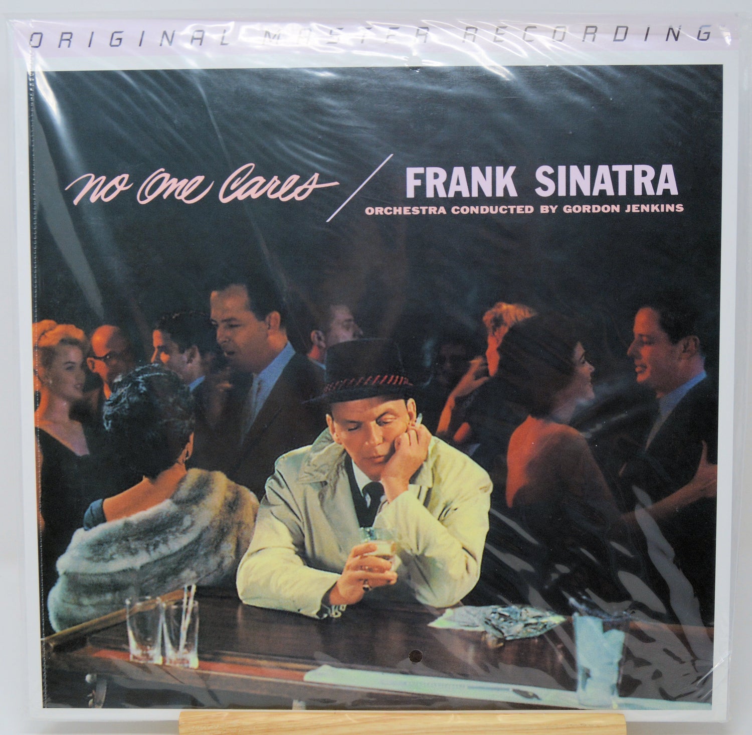 Vinyl record album cover for Frank Sinatra's 'No One Cares', sealed in plastic shrink wrap and displayed upright on a small wooden stand against a white background.