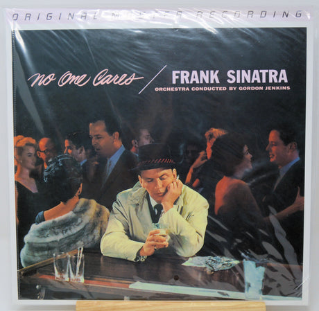 Vinyl record album cover for Frank Sinatra's 'No One Cares', sealed in plastic shrink wrap and displayed upright on a small wooden stand against a white background.