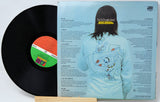 A vinyl record partially pulled from its jacket, showing the back cover artwork for The Stooges Band's 'Roots to End' album. The black record has a colorful orange, green, and white label, and the jacket features a light blue background with a graphic of a person wearing a light blue sweatshirt.