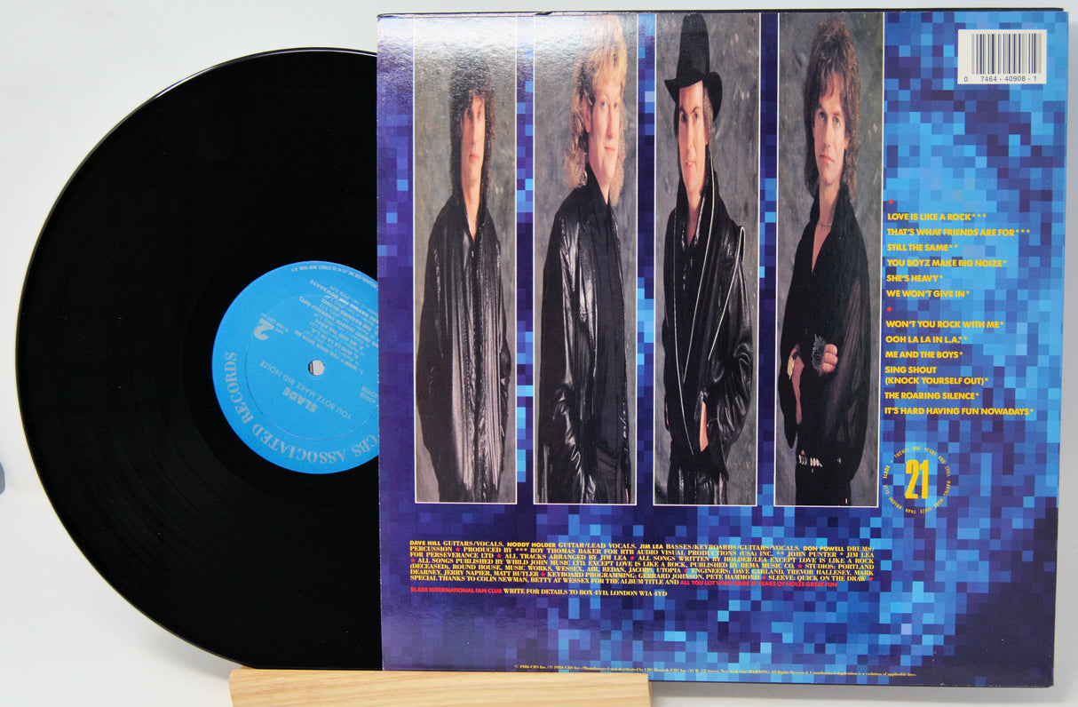 A vinyl record partially pulled from its sleeve, showing the black record with a blue center label and the back cover featuring four portrait photos of a band against a blue pixelated background.